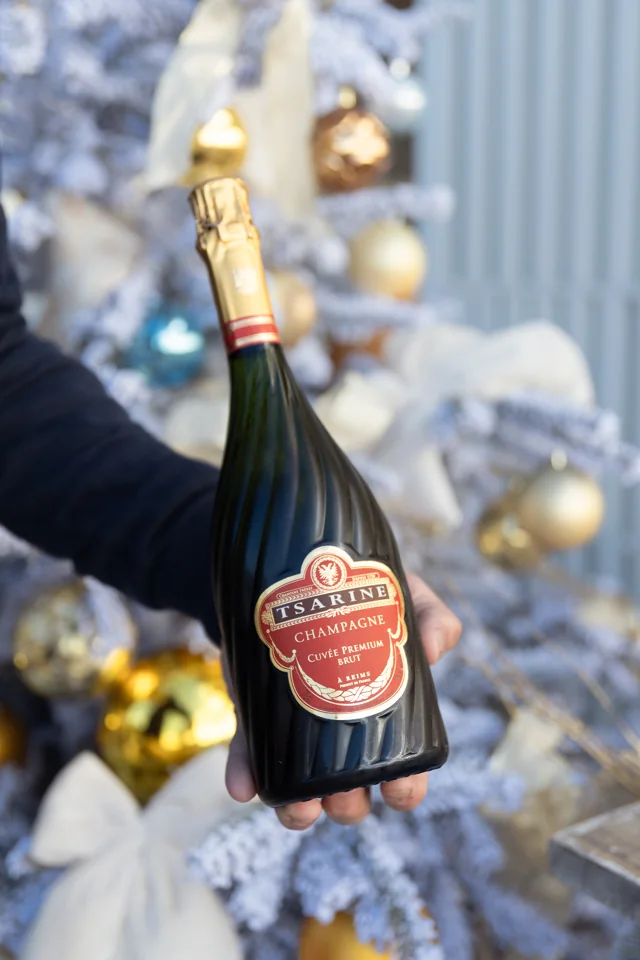 A hand presenting a Tsarine champagne bottle in front of softly focused festive decorations