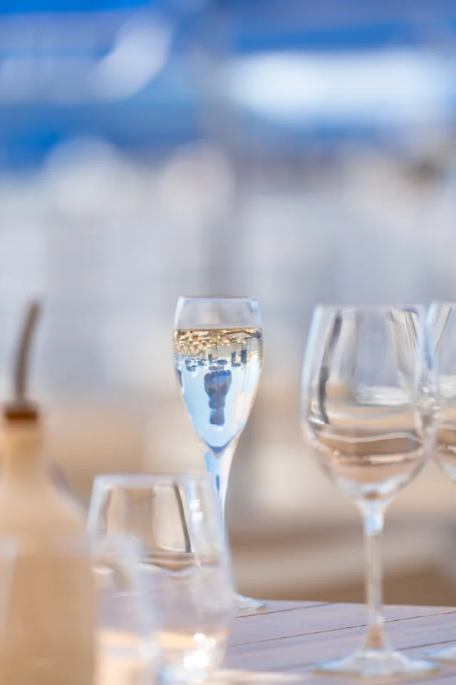 Champagne flute and glassware on a softly lit restaurant table with blue umbrellas beyond