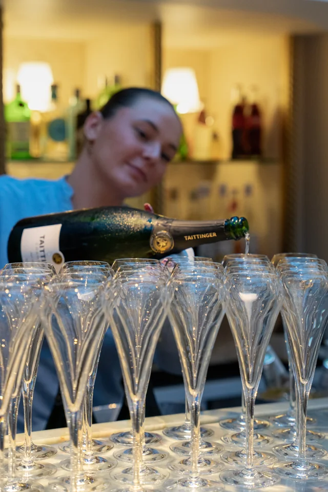 A server pouring champagne into rows of flutes at an indoor reception