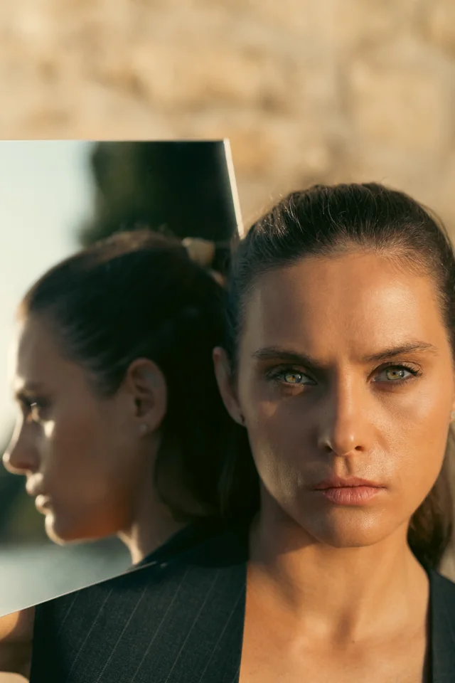 Woman in a dark jacket beside a mirror, in warm natural light